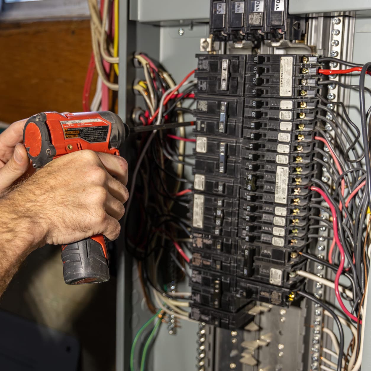 Electrician using an impact driver on breaker connections inside an open residential electrical panel